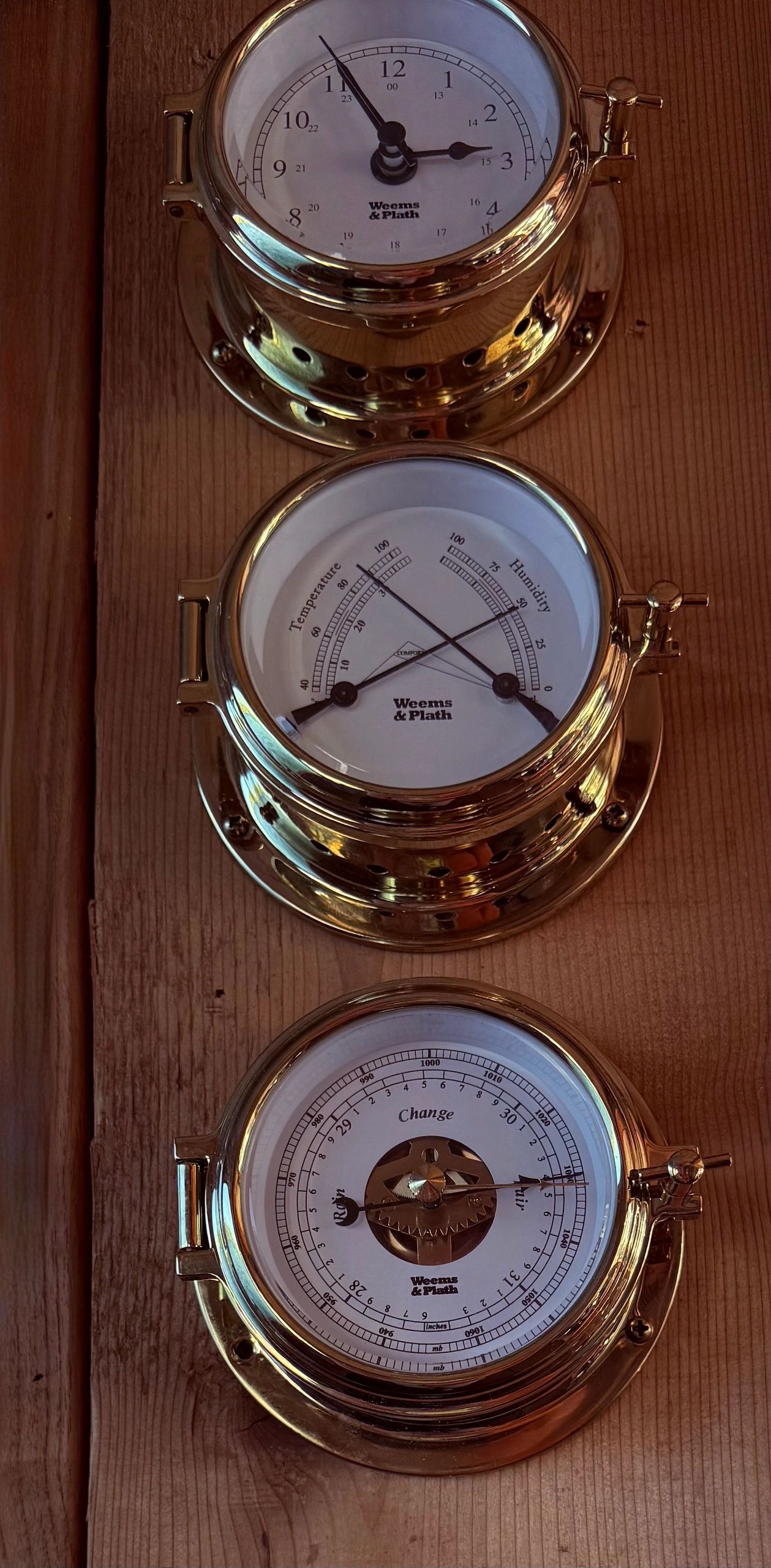 Brass ship's clock, thermometer, and barometer mounted on the cedar wall aboard Banya Boat