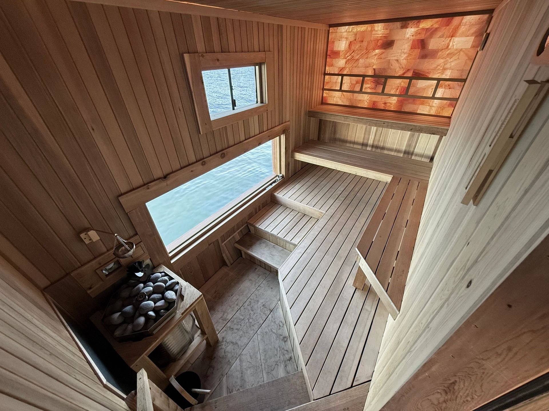 Cedar dry sauna interior with tiered benches, sauna stove, Himalayan salt wall, and a window over Lake Union